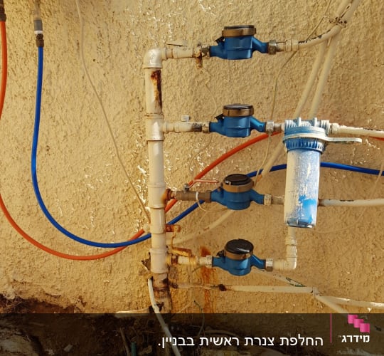 צנרת מים עם מדי מים כחולים על קיר חיצוני